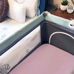 A pink fitted cot sheet in a baby cot next to a bed.