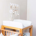Wooden crib with white mattress and baby mobile in a nursery setting with wooden mobile toys in white and cream with little goose theme