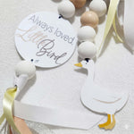 Baby wooden mobile toys beads and a tag reading 'Always loved, Little Bird' on a white background with little goose character