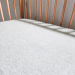 Close up of a grey melange baby cot sheet fitted on a mattress and resting inside a wooden baby cot.