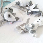A set of four handcrafted dingle dangle toys in a meadow animal theme in grey and whit: a bunny, bird, lamb, and butterfly. Made from soft felt with ribbons, designed for infant sensory development.