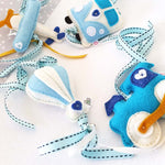 A set of four handcrafted dingle dangle toys in transport theme in blues: a train, hot air baloon, volksie, and plane. Made from soft felt with ribbons, designed for infant sensory development.