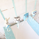 A set of four handcrafted dingle dangle toys in woodland animal shapes in shades of blue: a rabbit, an owl, a bear, and a deer. Made from soft felt with ribbons, designed for infant sensory development.
