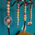 Decorative hanging items with beads and record and tape design against a teal background