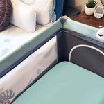 A green fitted cot sheet in a cot next to a bed