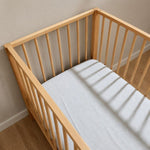 Birds eye view of a grey melange baby cot sheet fitted on a mattress and resting inside a wooden baby cot.