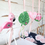 A set of four handcrafted dingle dangle toys in a flamingo theme in pinks and greens: a flamingo, leaf, heart, and protea. Made from soft felt with ribbons, designed for infant sensory development.