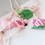A set of four handcrafted dingle dangle toys in a flamingo theme in pinks and greens: a flamingo, leaf, heart, and protea. Made from soft felt with ribbons, designed for infant sensory development.